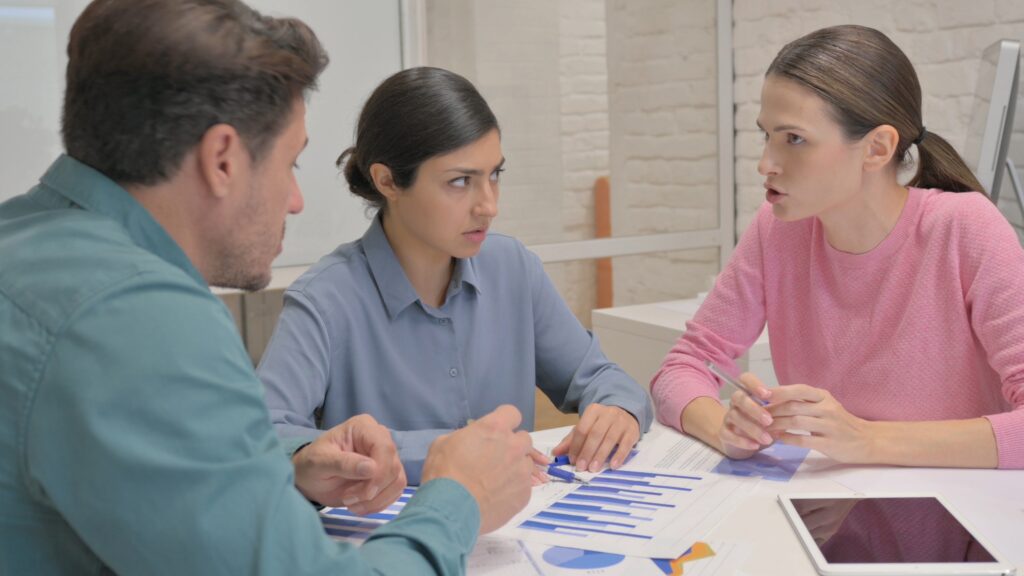 Team reviewing documents and making decisions under pressure during a meeting, with hands pointing and discussing options